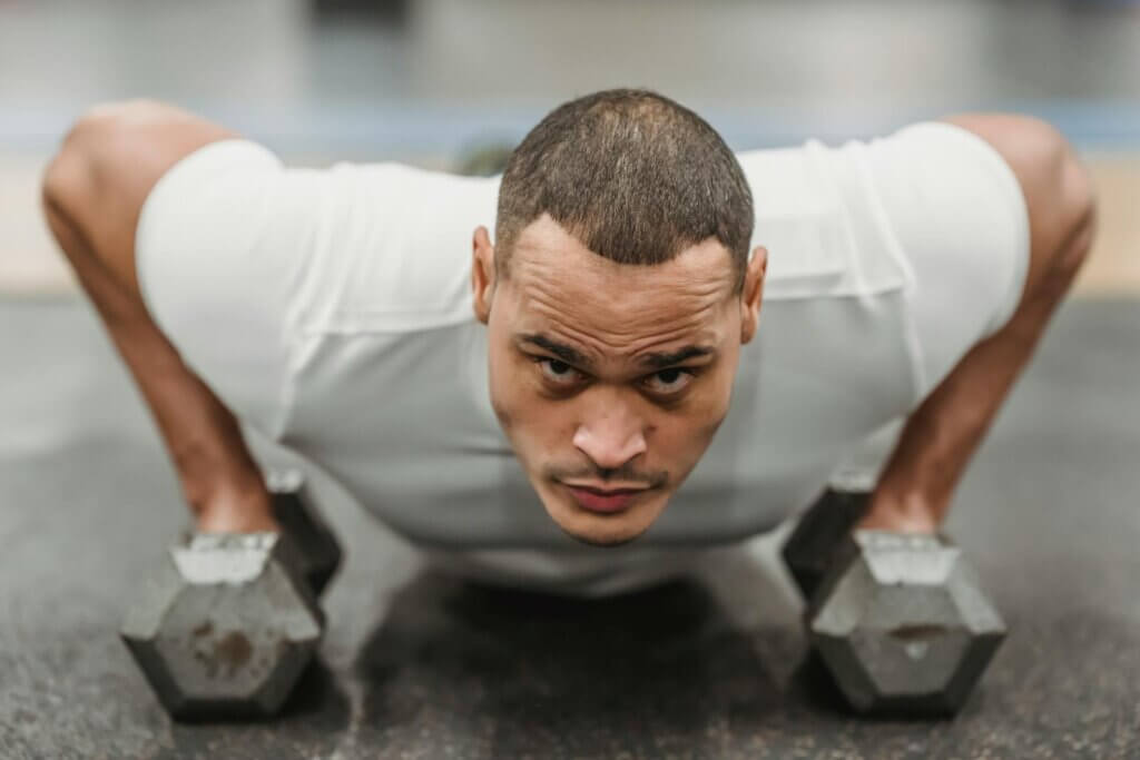 Focused ethnic man doing push up with dumbbells